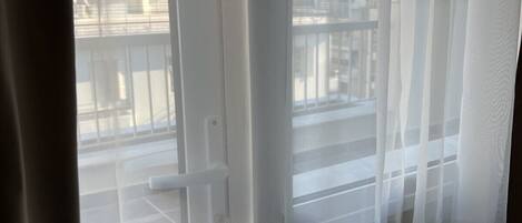 A view through a window with a view of a cityscape, including buildings and a balcony.