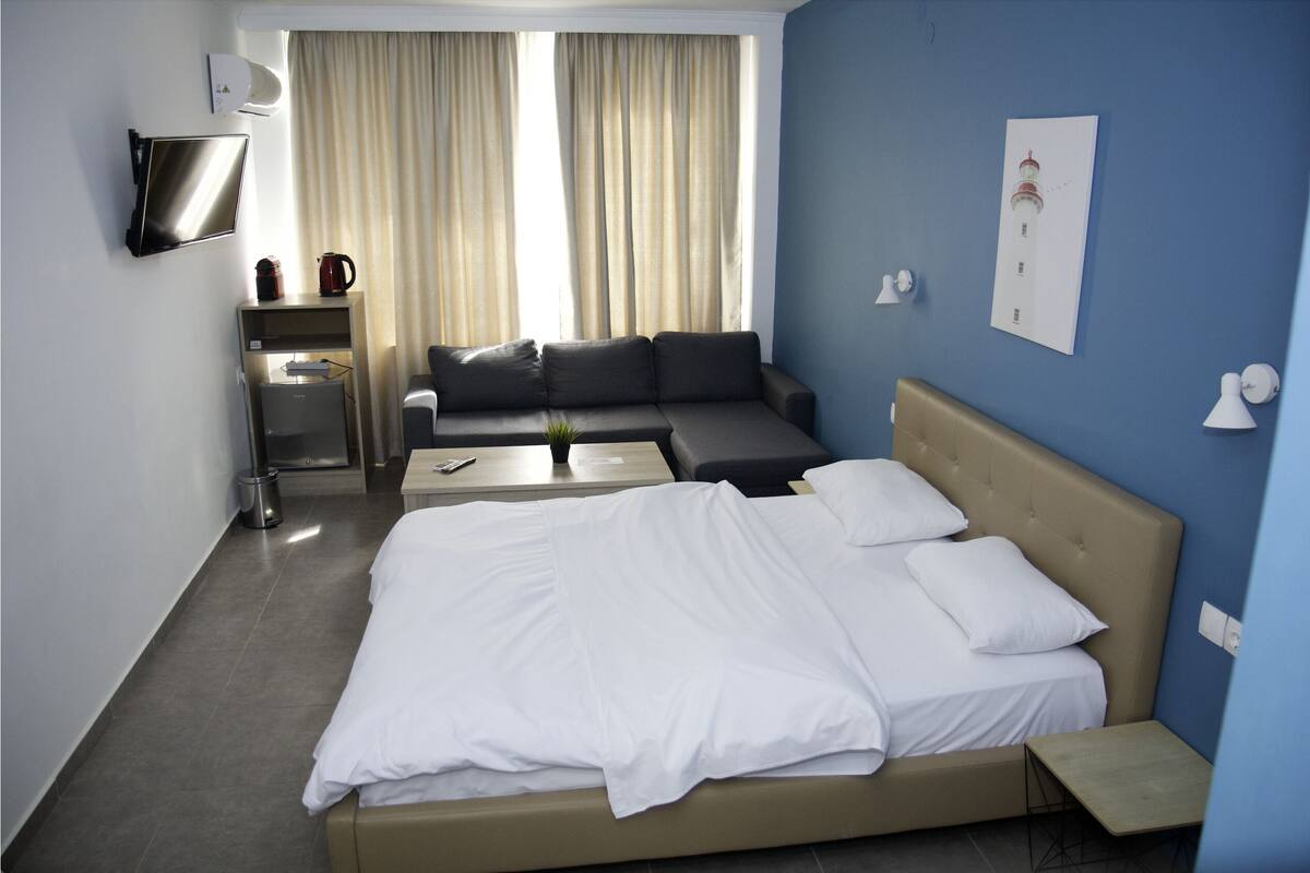 Habitación de hotel con cama, sofá, televisión, cafetera y una pequeña mesa.