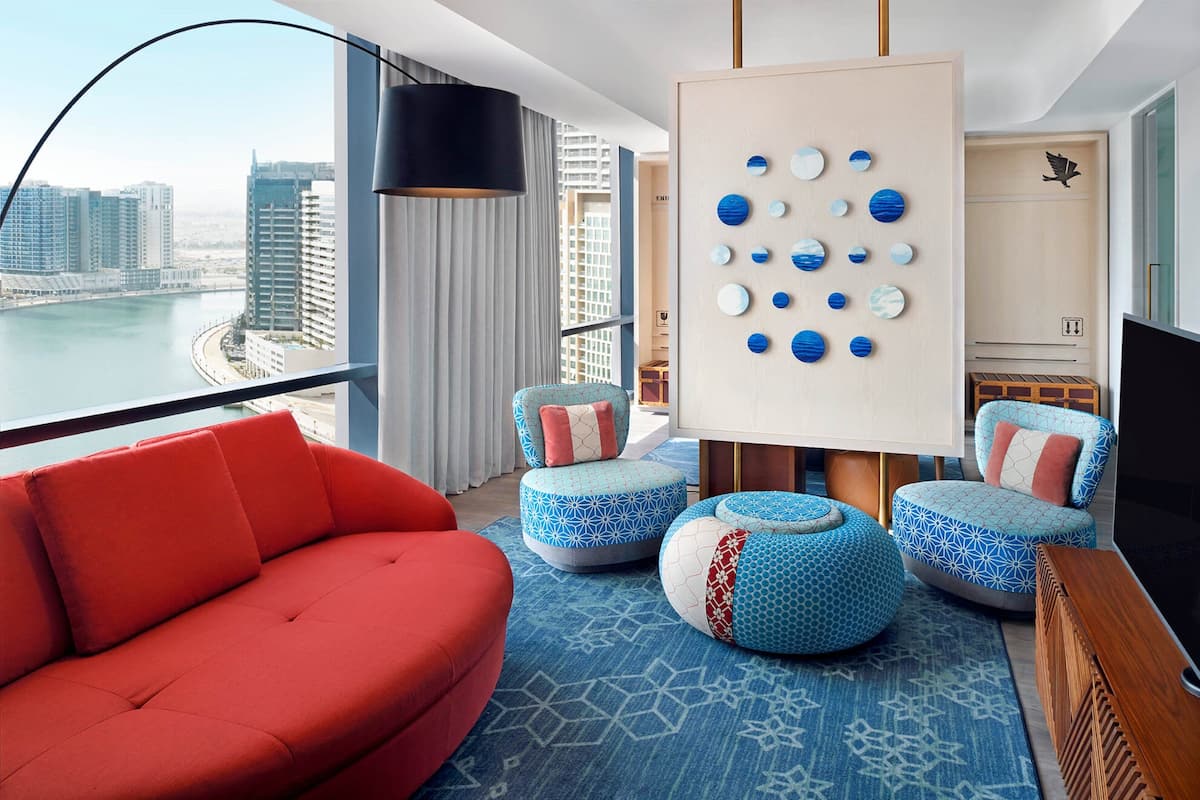 Una sala de estar moderna con un sofá rojo, otomanas estampadas en azul, vistas a la ciudad y una obra de arte en la pared.