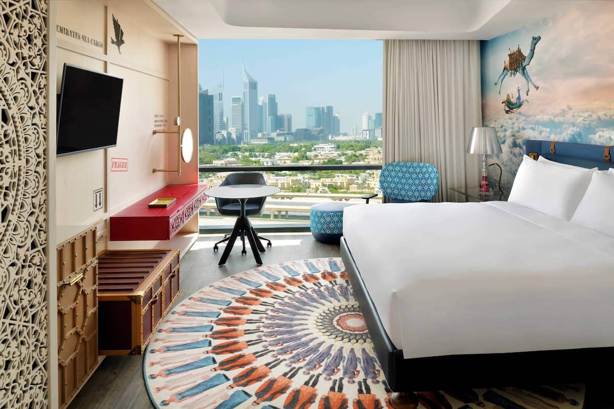 Ein Hotelzimmer mit Bett, Schreibtisch, Stuhl, Fernseher und Blick auf die Stadt, inklusive dekorativer Wand.