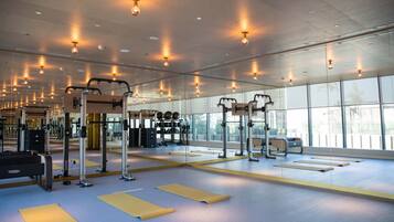 Un gimnasio con equipo de ejercicio, espejos y ventanas amplias.