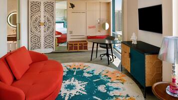 Una habitación de hotel moderna con un sofá rojo, una mesa redonda, un televisor y un panel decorativo en la pared.