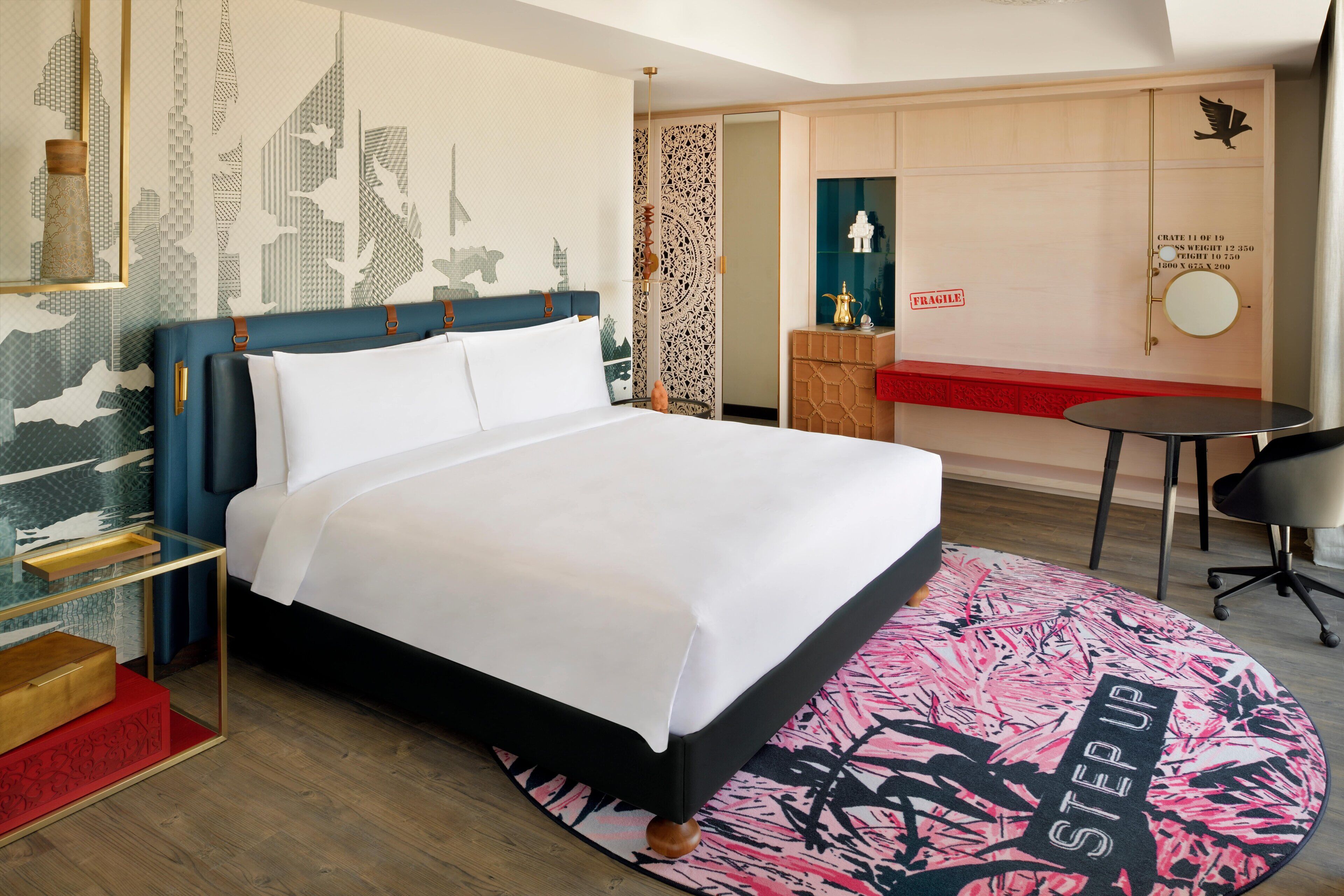 A hotel room with a bed, a desk, a chair, a patterned rug, and a decorative wall.