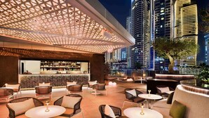 Un bar situé sur un toit, offrant une vue panoramique sur la ville, avec des places assises en plein air et un espace bar où sont exposées de nombreuses bouteilles sur des étagères.