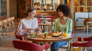 Deux personnes sont assises à une table dans un restaurant au décor moderne, avec des chaises en bois et une variété de plats proposés.