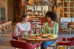 Zwei Personen essen an einem Tisch in einem Restaurant mit modernem Ambiente, Holzstühlen und verschiedenen Speisen.
