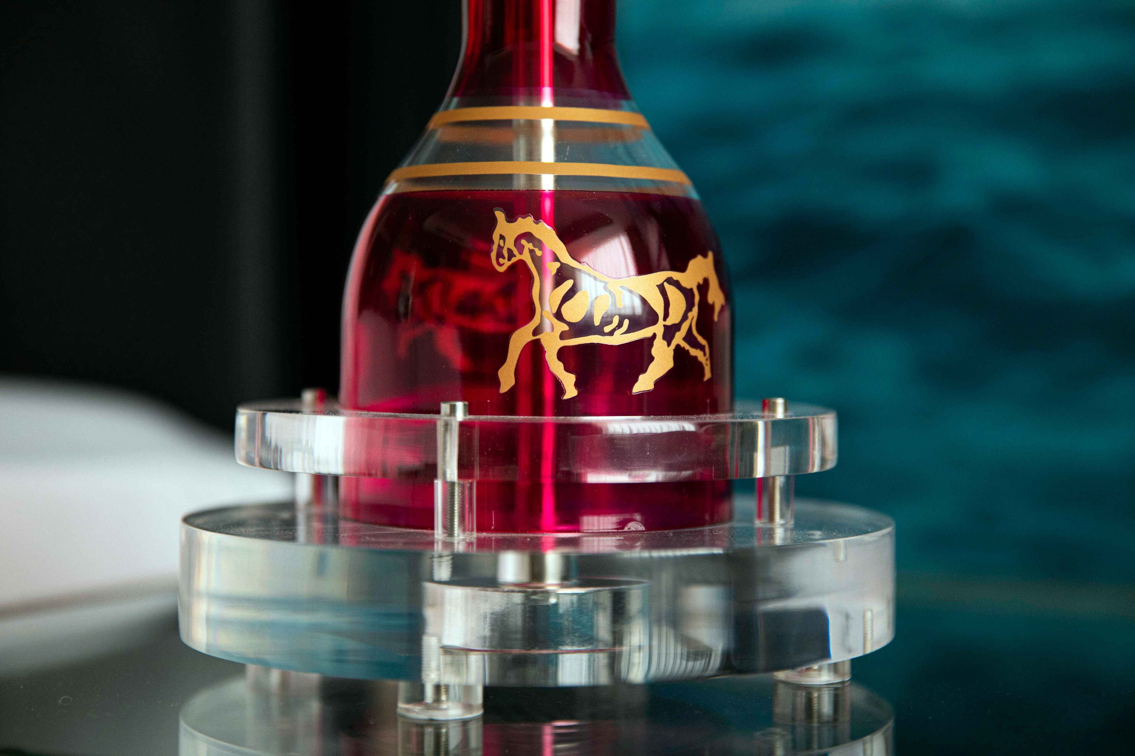 A red vase with a gold horse design on a clear stand.