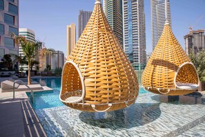 A swimming pool area with hanging chairs and high-rise buildings in the background.