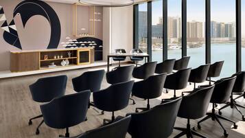 A conference room with a view of a marina and buildings, featuring a modern design with black chairs and a wooden console.