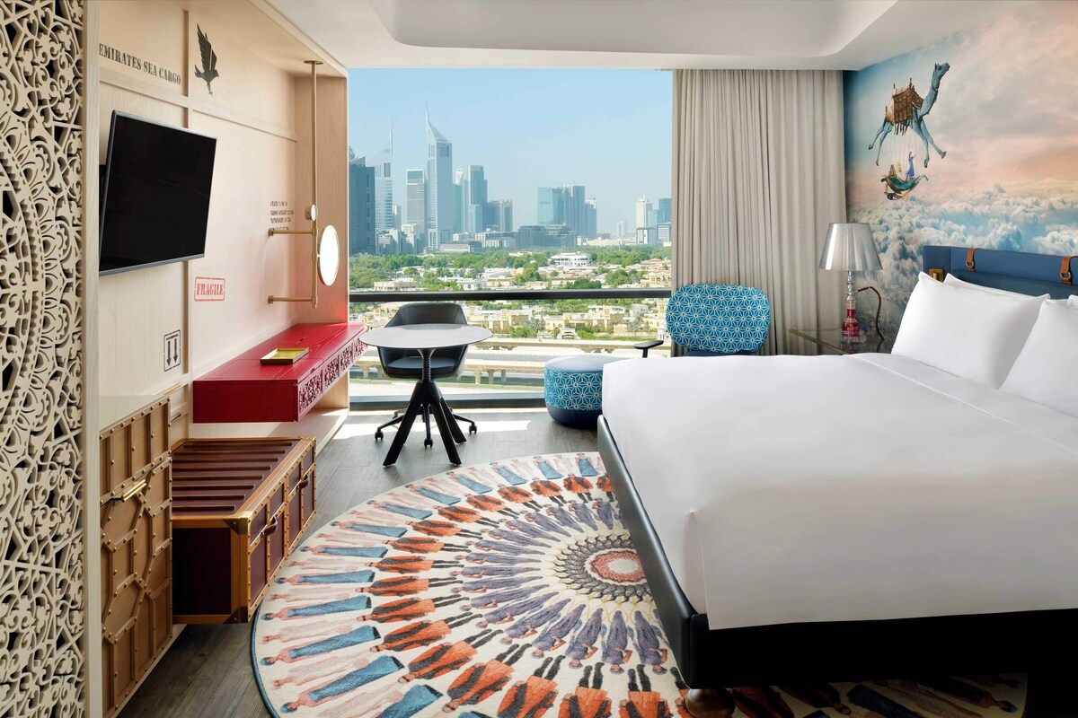 Ein Hotelzimmer mit Bett, Schreibtisch, Stuhl, Fernseher und Blick auf die Stadt, inklusive dekorativer Wand.