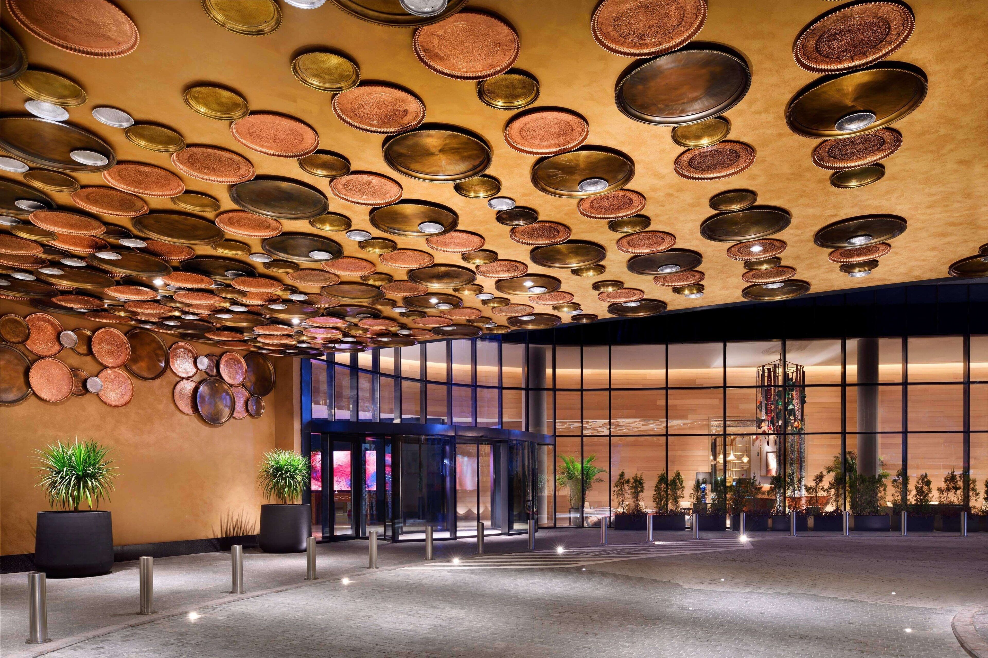 A hotel lobby with a patterned ceiling, large windows, and potted plants.