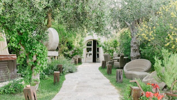 A stone pathway leading to a rustic entrance with a wooden door, surrounded by lush greenery and outdoor furniture. - B&B Barone Gambadoro (Monte Sant'Angelo)