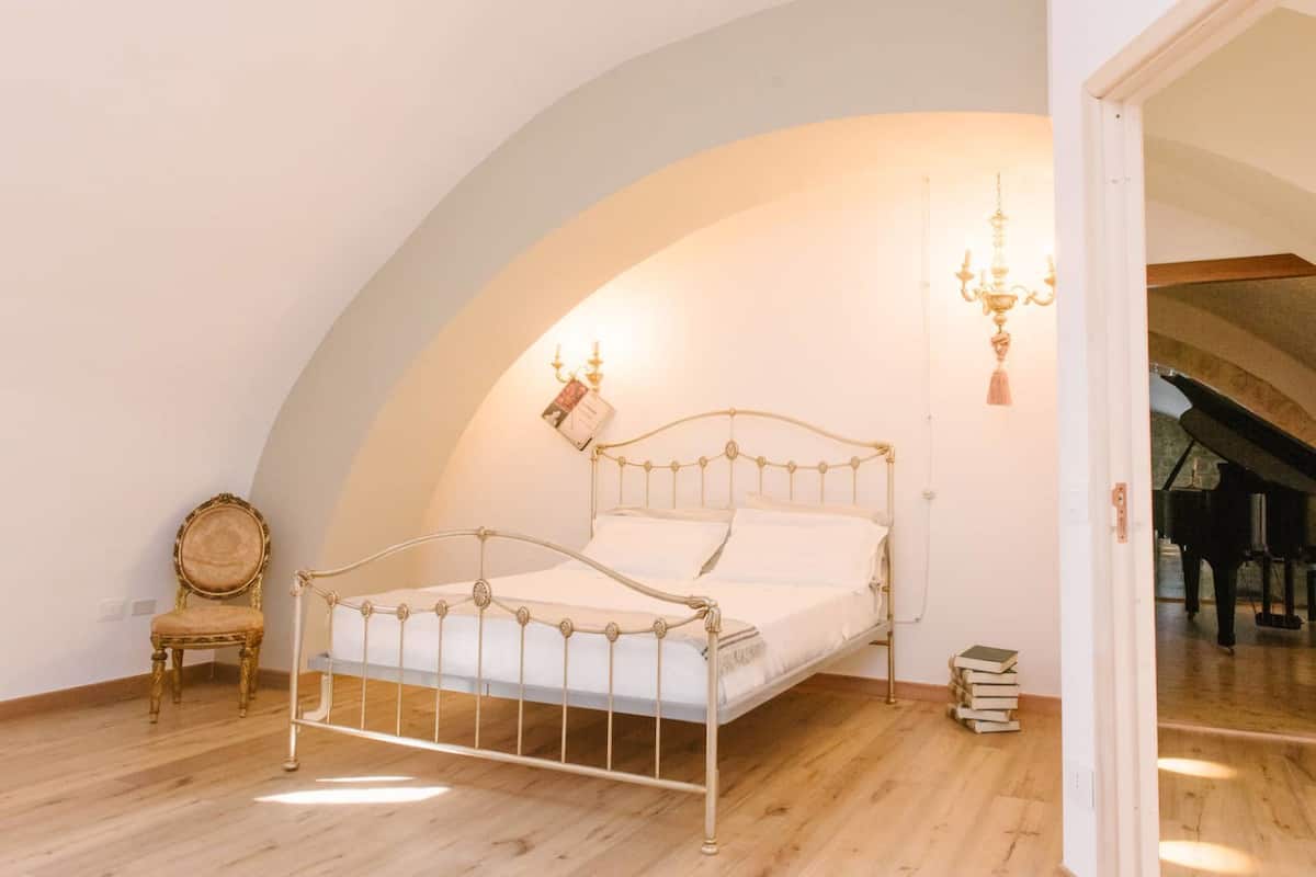 A bedroom with a metal bed frame, a wooden chair, and a chandelier.