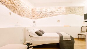 A bedroom with a stone wall, a bed with pillows, a chair, and a bedside table. - B&B Barone Gambadoro (Monte Sant'Angelo)