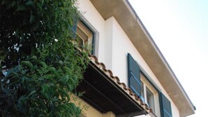 Un edificio de dos pisos con fachada blanca, contraventanas verdes y un pequeño balcón.