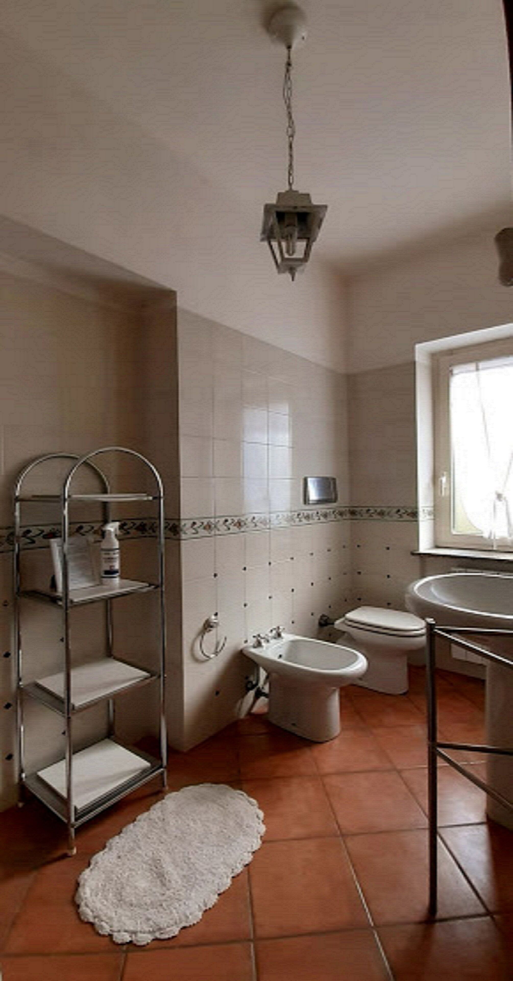 A bathroom with a toilet, bidet, sink, and shelves with toiletries.