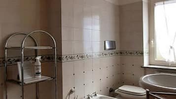 A bathroom with a toilet, bidet, sink, and shelves with toiletries.