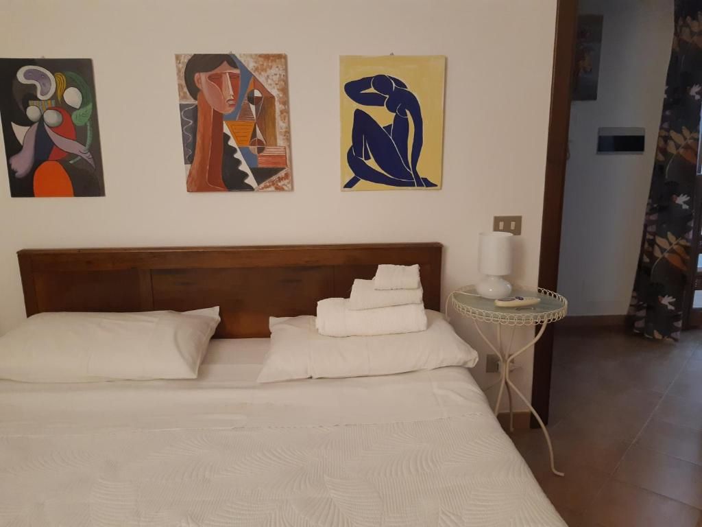 Una habitación de hotel con una cama, una mesita de noche con lámpara y tres cuadros abstractos en la pared.