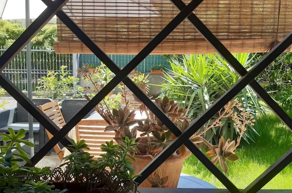 Un patio al aire libre con mesa y sillas, rodeado de plantas en macetas y una pérgola de bambú.