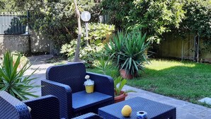 Un área de estar al aire libre con mobiliario de mimbre, una planta en maceta y una mesita con un bol y un limón.