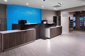 Een receptiegedeelte met een blauwe wand met patroon, een 'Corner Market' bord en een koelkast gevuld met drankjes.