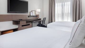 Una habitación de hotel con una cama grande, un escritorio con una silla, un televisor de pantalla plana montado en la pared y una ventana con cortinas.