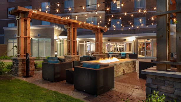 Een terras buiten met stenen vloer, houten pergola en zitplaatsen.