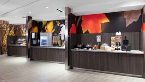 Een moderne receptiebalie met een koffieapparaat, koelkast en een toonbank met diverse etenswaren.