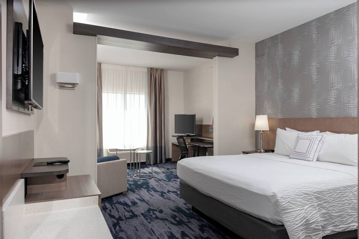 Ein Hotelzimmer mit einem großen Bett, einem Schreibtisch, einem Fernseher und einer Sitzecke mit Blick ins Freie.