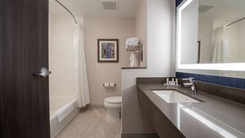 A modern bathroom with a bathtub, toilet, and a large mirror.