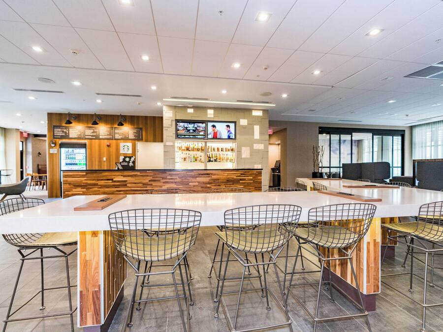 A modern bar area with a long counter, multiple screens, and a seating area with metal chairs.