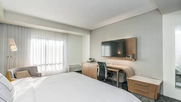 Habitación de hotel con una cama grande, un escritorio con una silla, una televisión y una lámpara.