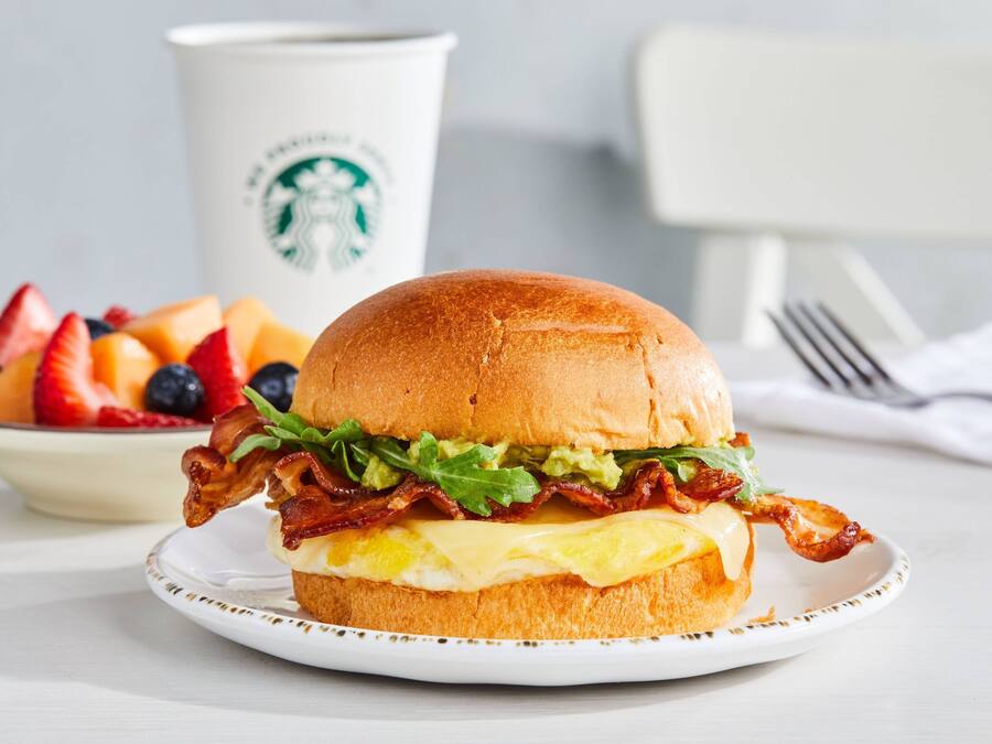 A breakfast sandwich on a plate with a Starbucks cup in the background.