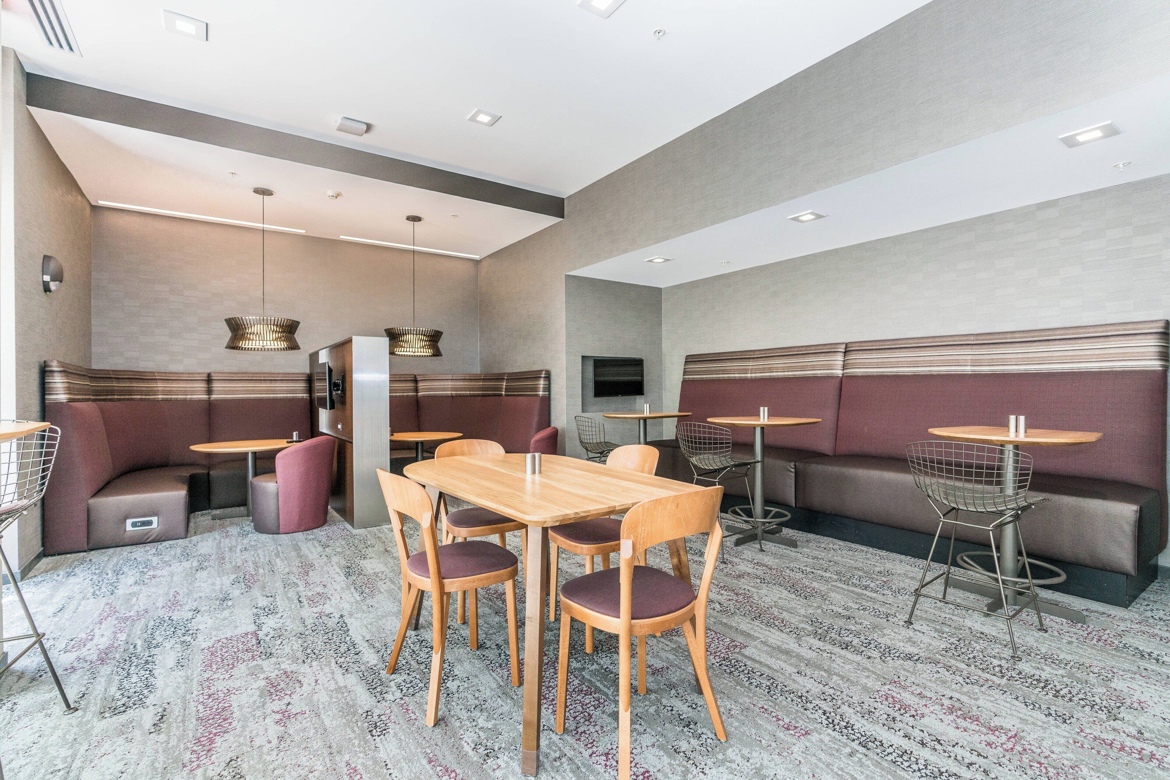 A modern restaurant with booth seating, wooden tables, and a patterned carpet.