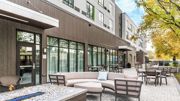 An outdoor patio area with seating, a fire feature, and a view of the building's exterior. - Courtyard by Marriott West Springfield (West Springfield)