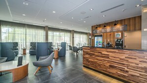 A modern reception area with a wooden reception desk, seating area with sofas and chairs, and large windows providing natural light. - Courtyard by Marriott West Springfield (West Springfield)