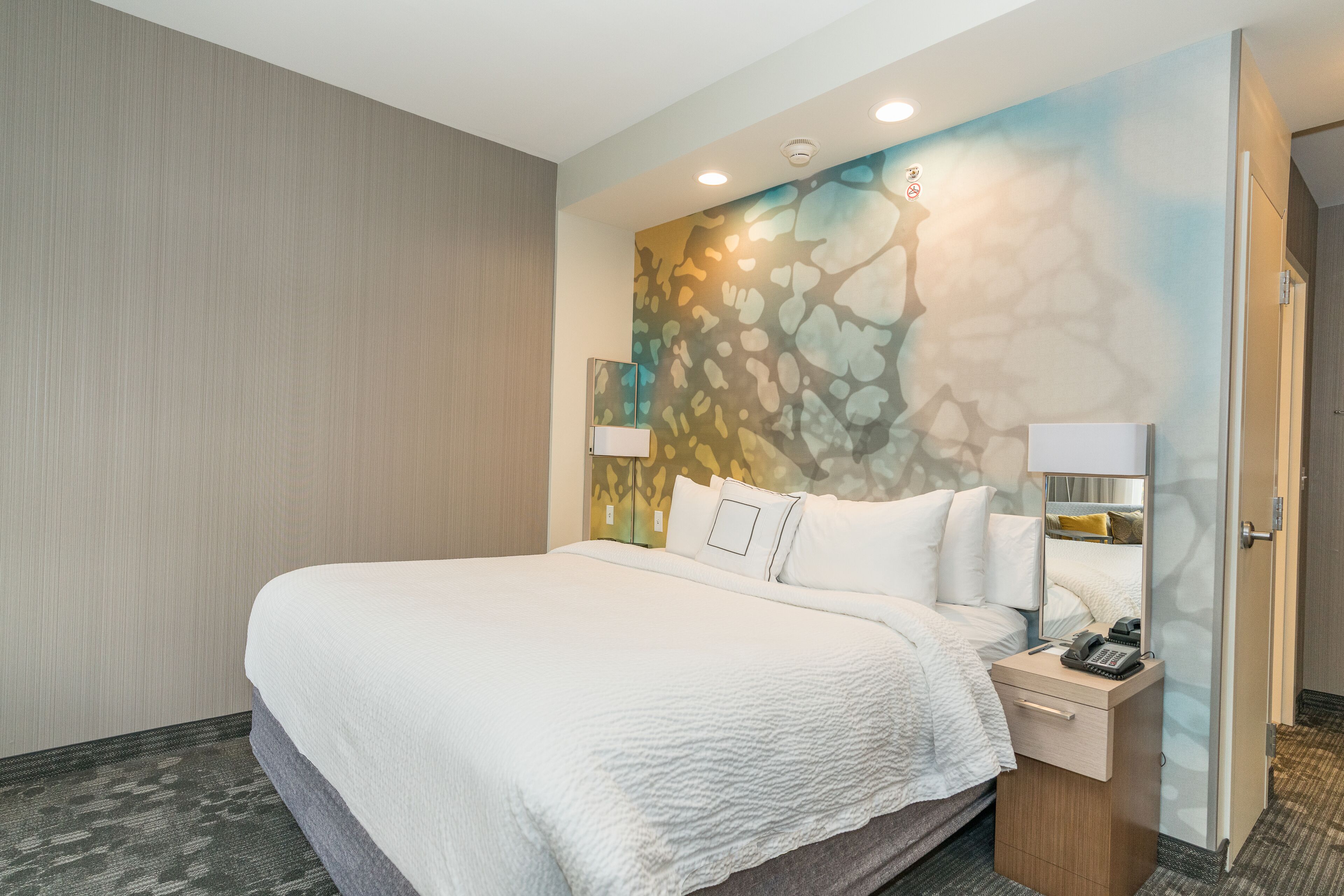 A hotel room with a large bed, a nightstand with a lamp, and a wall mural.