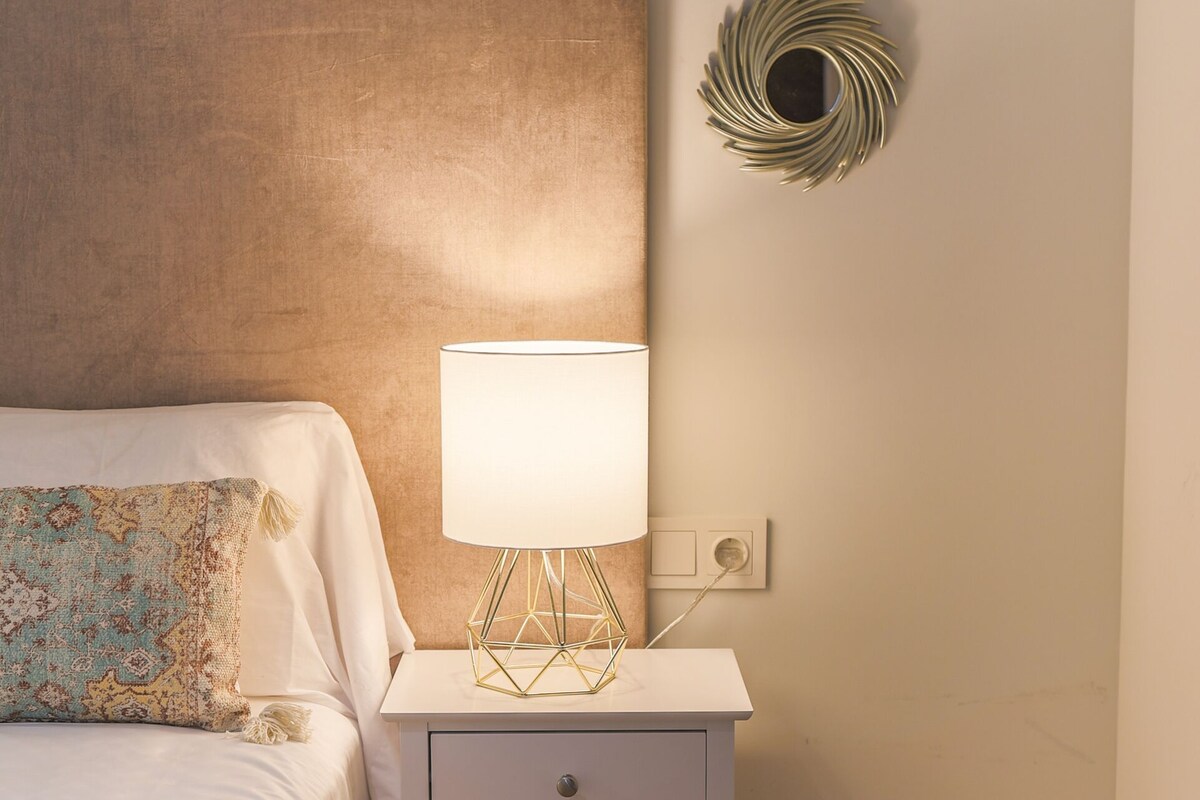 A bedroom with a bed, a bedside table with a lamp, and decorative wall art.