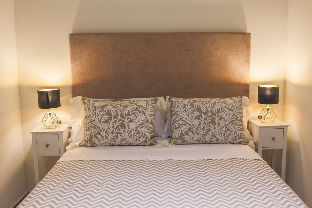 A bed with a patterned bedspread, two matching pillows, and two bedside lamps on nightstands.