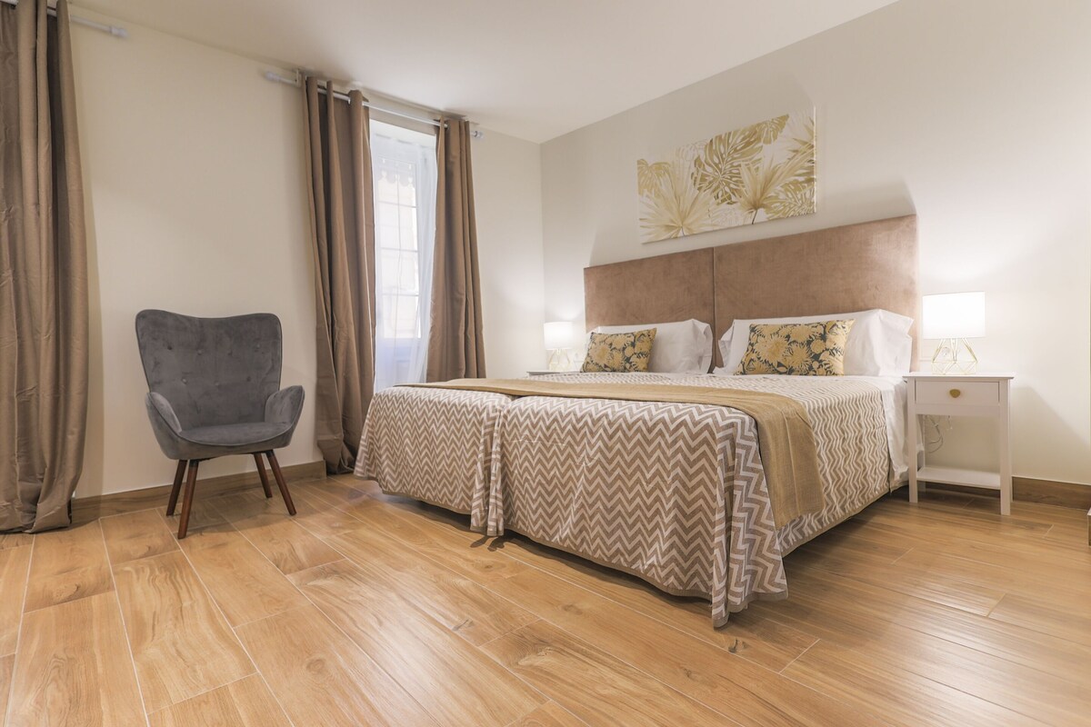 A bedroom with a bed, a chair, a nightstand, and a window with curtains.