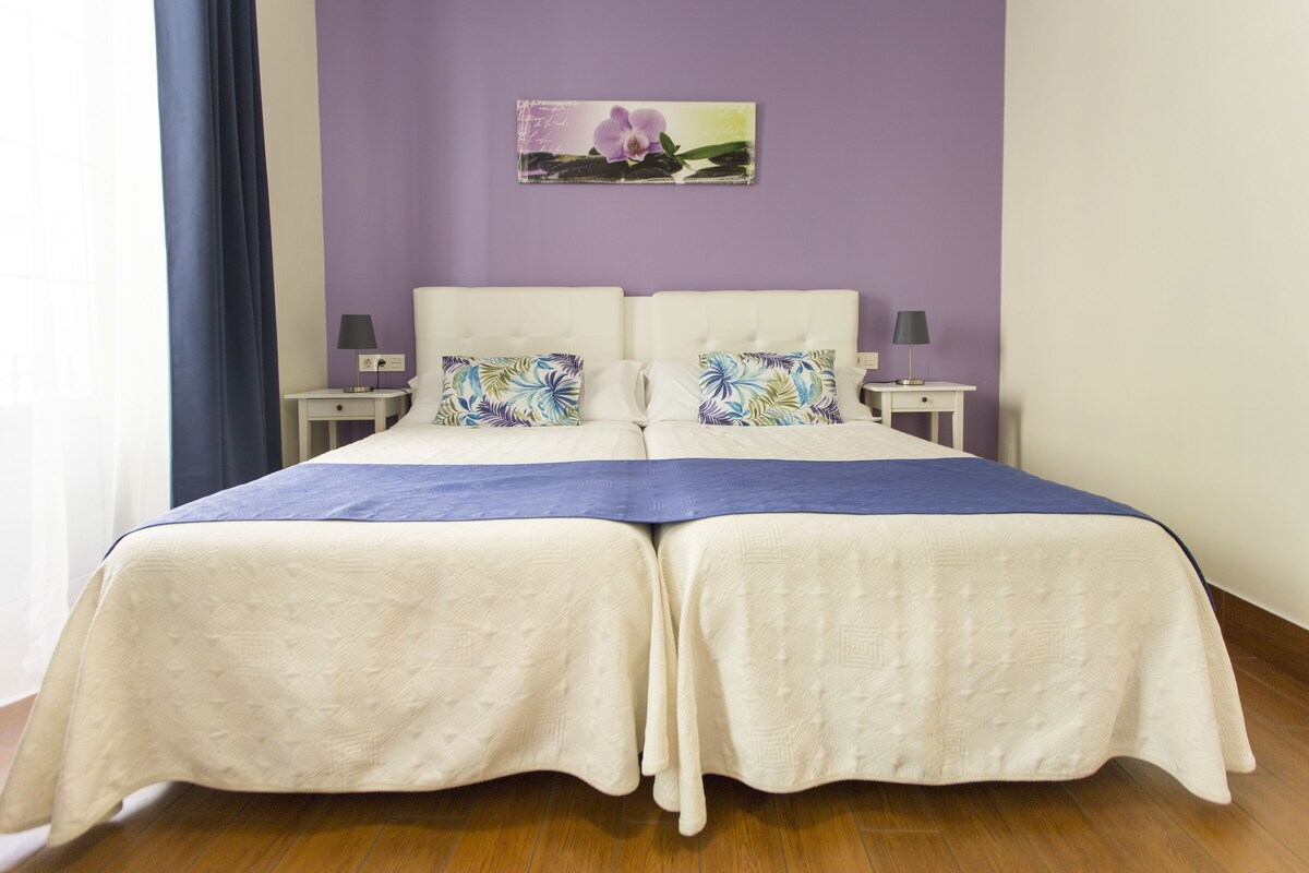 A double bed with a white headboard and two nightstands, each with a lamp.