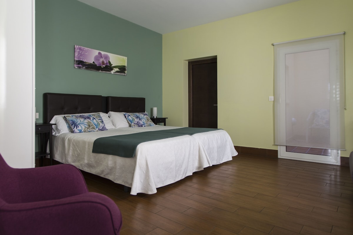 A bedroom with a bed, a nightstand, a chair, a door, and a window.