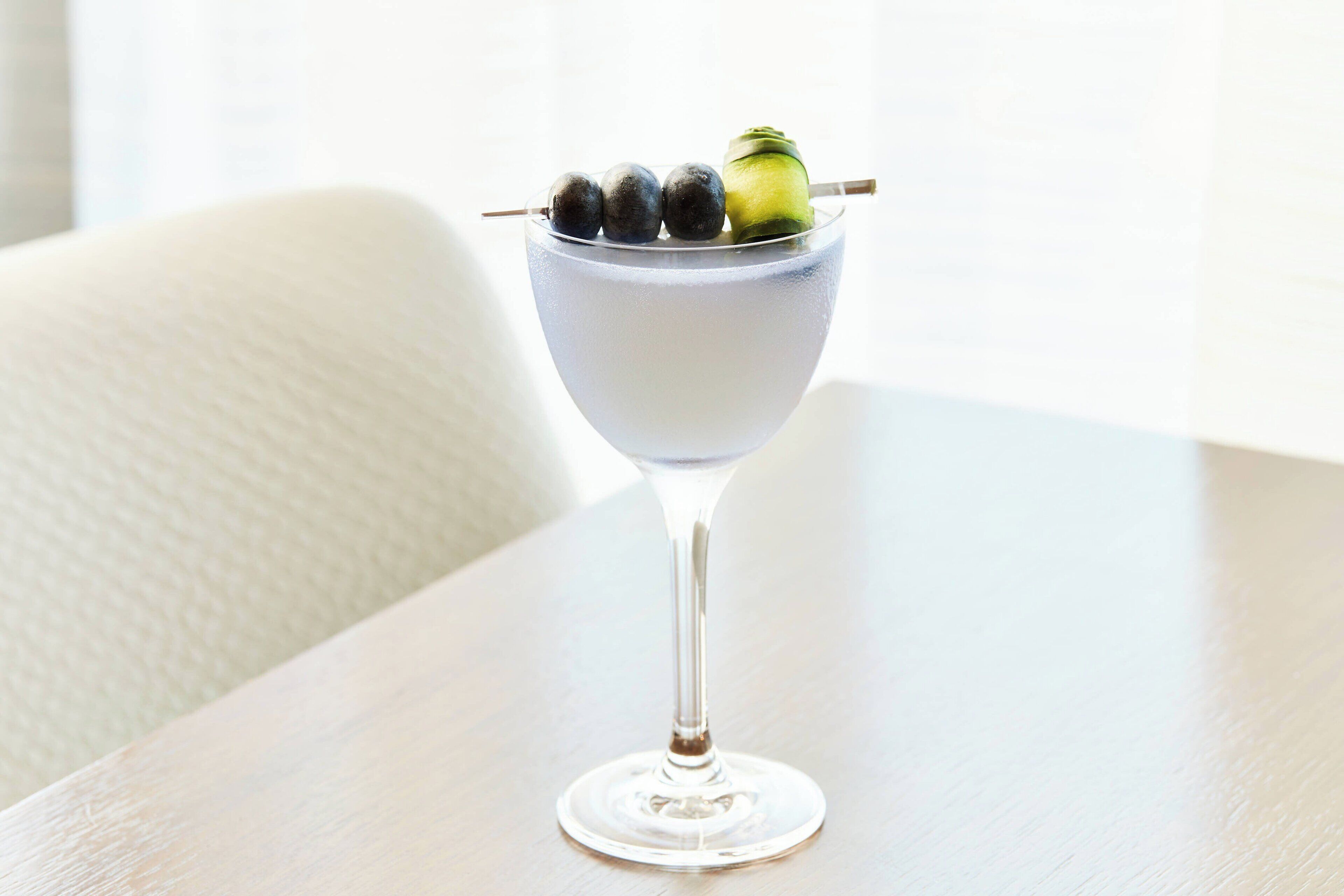A clear glass cocktail with a garnish on a wooden table.