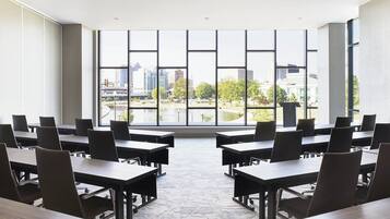 A conference room with tables and chairs arranged for meetings, large windows offering a view of a cityscape.
