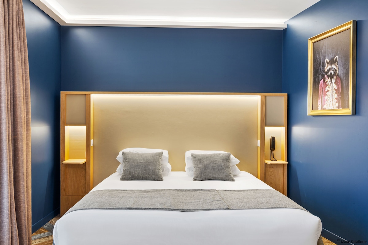 Een hotelkamer met een groot bed, twee nachtkastjes met lampen, een hoofdbord met ingebouwde verlichting en een ingelijst schilderij aan de muur.