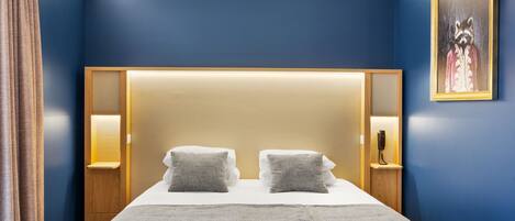 A hotel room with a large bed, two bedside tables with lamps, a headboard with integrated lighting, and a framed picture on the wall.