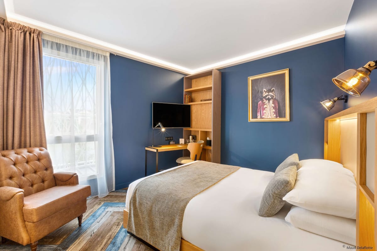 Une chambre d’hôtel avec un lit, un bureau, une chaise, une télévision et un tableau au mur.