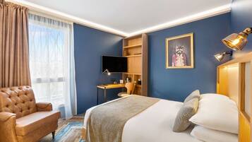 Habitación de hotel con cama, escritorio, silla, televisor y un cuadro en la pared.