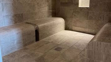A room with a tiled floor and walls, a window with a view, and a bench along one wall.