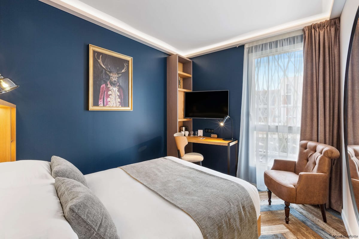 Une chambre d’hôtel avec un lit, un bureau avec un ordinateur, une télévision et une chaise.